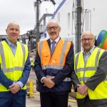 Port director Mike Sellers, Brittany Ferries chief executive Christophe Mathieu, and Portsmouth City Council leader Cllr Steve Pitt stand in a line, all wearing high-visibility vests, in front of a Brittany Ferries ship which is plugged into the shore power system